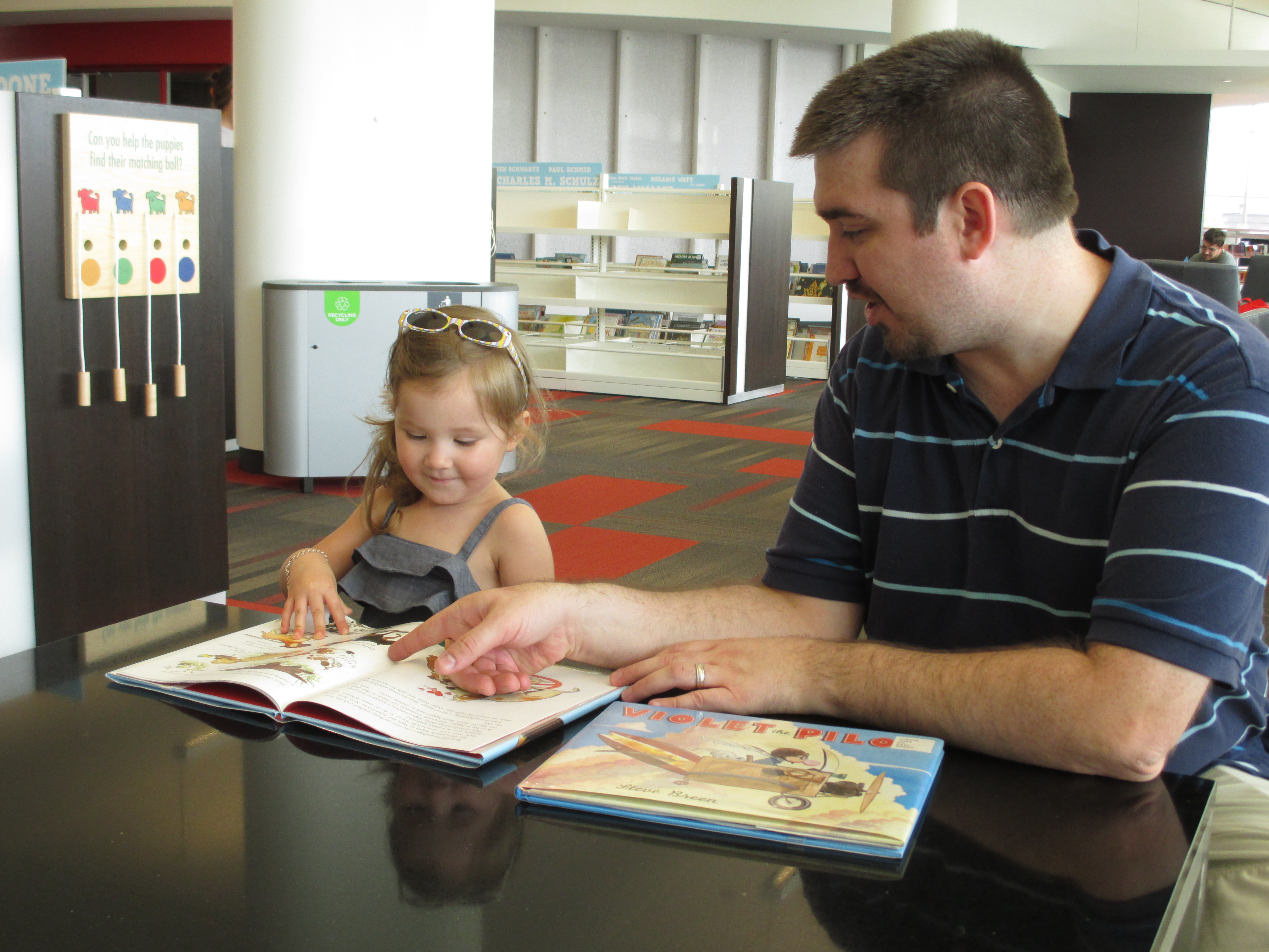 Father and daughter reading together at a library table