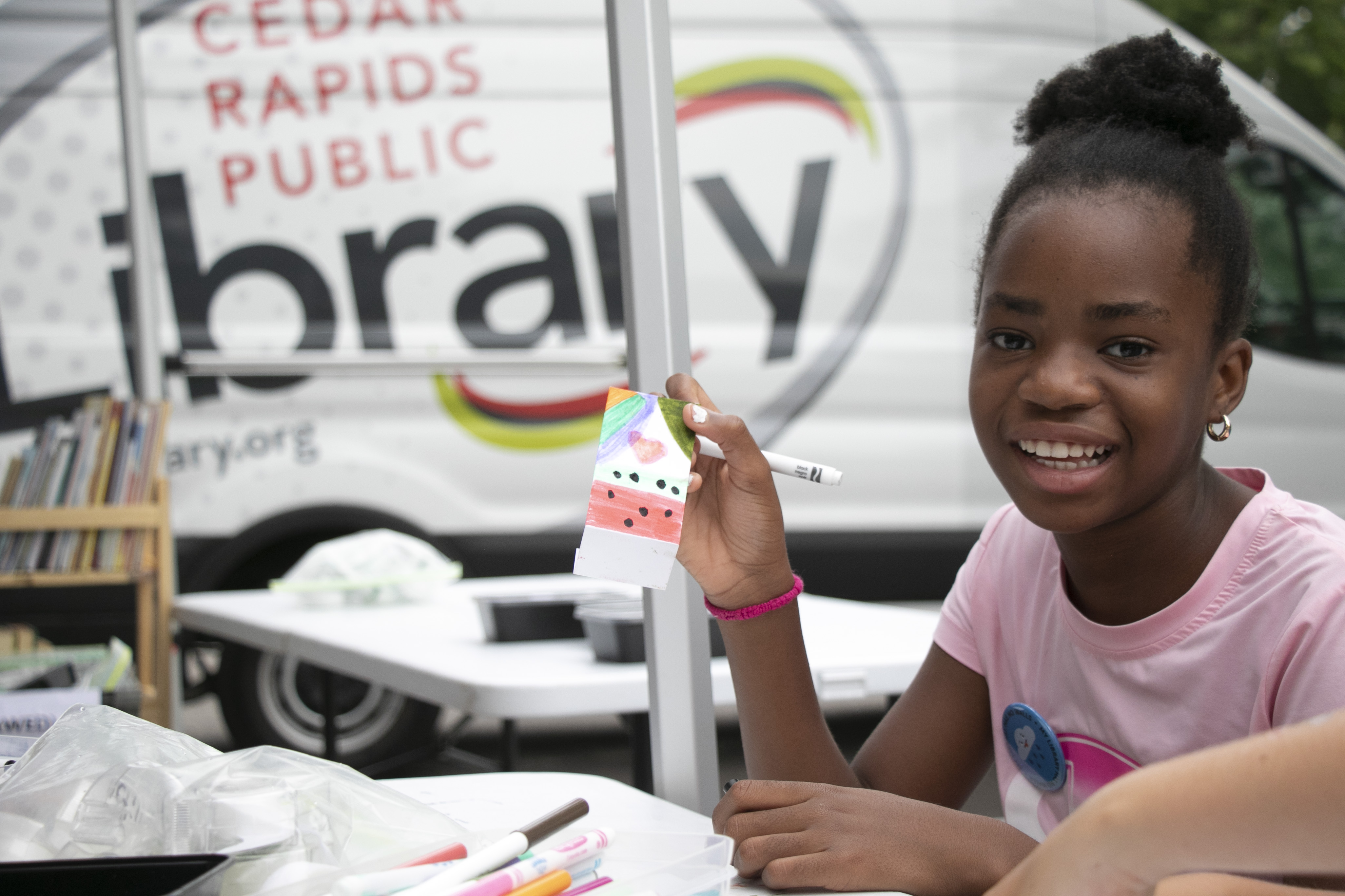 A girl smiles while holding a craft in front of the Mobile Technology Lab.