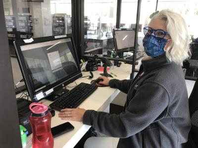 A woman in a blue face fast and black sweatshirt sits at a computer.