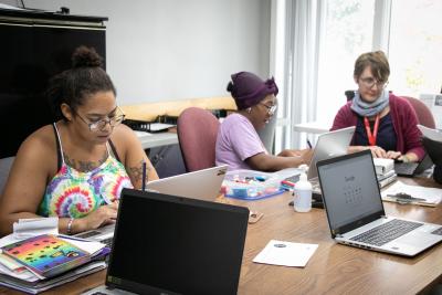 Three women look at laptops together.