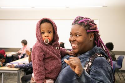 A woman holding a baby smiles at the child.