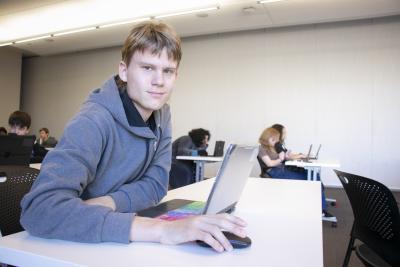 A teen boy looks at the camera while working on a laptop.