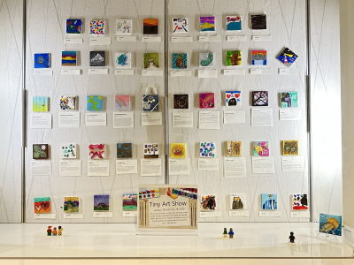 Tiny art canvases hang on a gallery wall.