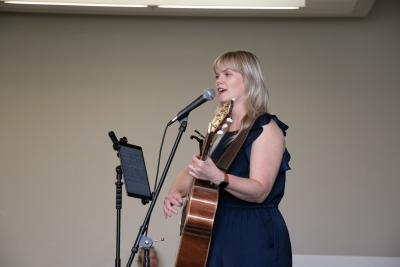 A woman holding a guitar sings into a microphone.