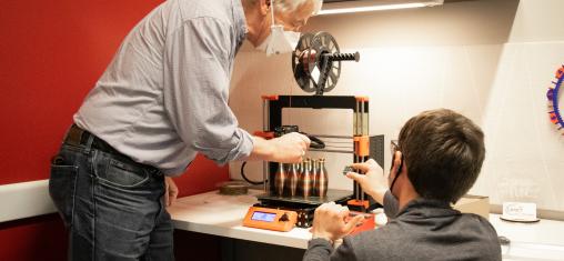 A man and woman lean over a 3D printer.