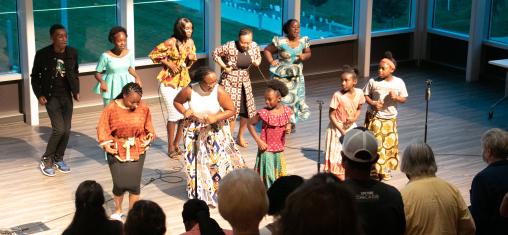 A choir of people in African clothing dance in front of a crowd in Whipple Auditorium in the Downtown Library.