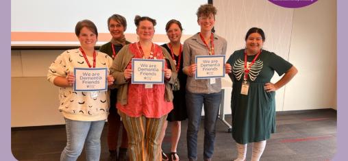 A group of people smile at the camera while holding certificates saying they are Dementia Friends.