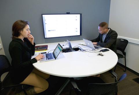 Technology Conference Room with two people working on laptops at a table in front of a Smart TV screen