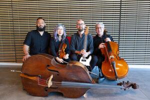 Four musicians seated together holding a violin, cello, electric guitar, and upright bass.